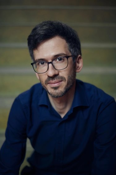 Lukas Linder, ein Mann mit blauem Hemd und Brille, schaut in die Kamera
