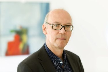 Martin Hielscher in einem schwarzen Sakko mit dunkelblauem Hemd schaut direkt in die Kamera